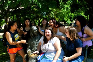 group of laughing students sit with John Lennon statue